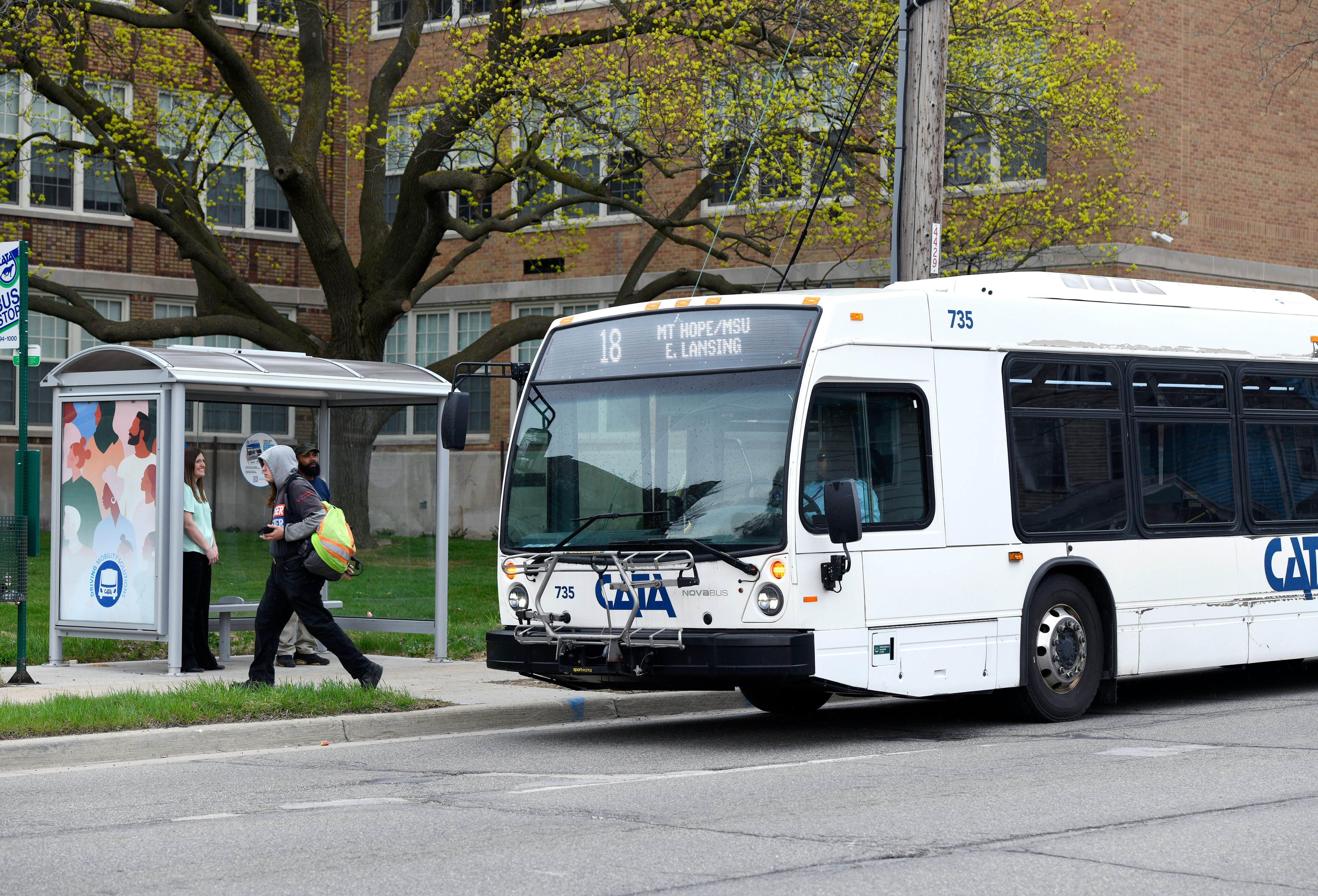  CATA Route 18 bus to Mt. Hope/MSU arriving at a bus stop shelter with passengers waiting to board