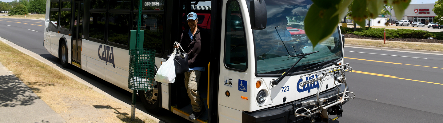 Person getting off a CATA city bus at a roadside bus stop carrying shopping bags.