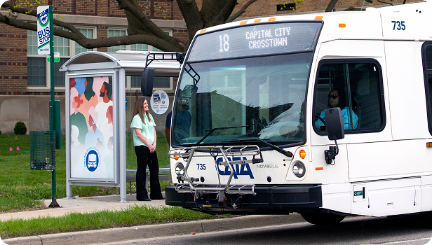 Woman waiting at a bus stop as a city bus arrives.