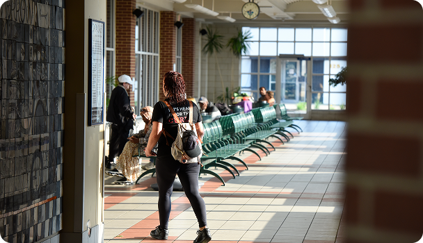 Woman checking a transit schedule board in a station waiting area with benches and passengers