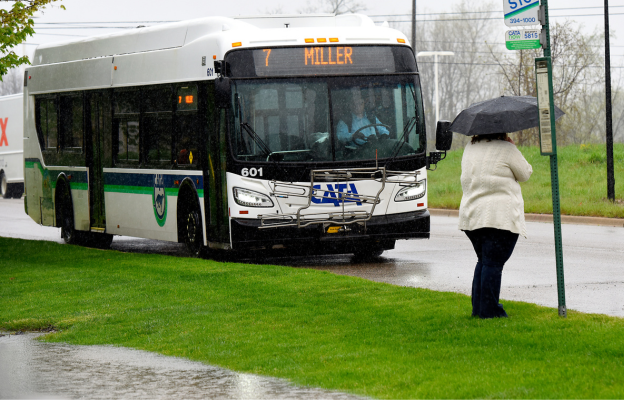 A woman with an umbrella waiting for the bus in the rain