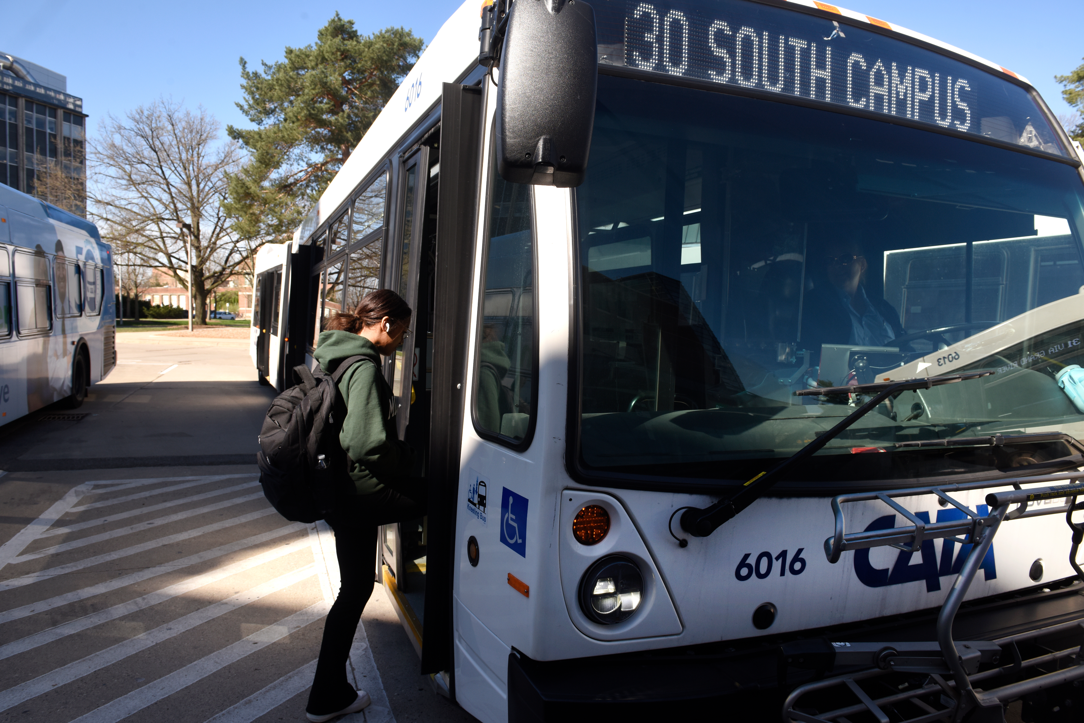 Passenger with a backpack boarding a CATA bus displaying ‘30 South Campus,’ with the driver visible inside and another bus parked nearby.